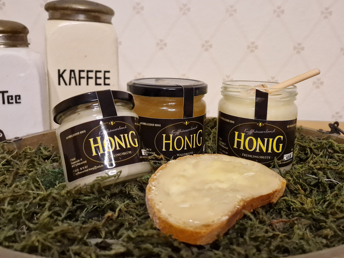 Frontansicht von drei Gläsern feincremigen Honigs. Ein Brot mit Honig bestrichen.